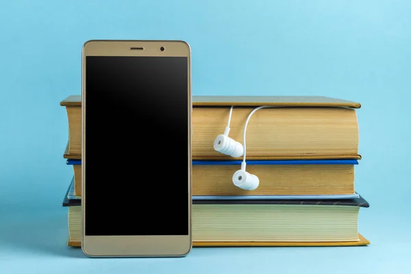 Headphones, mobile phone and books on a blue background. Audio book concept. Play audio playback of literary, educational books.