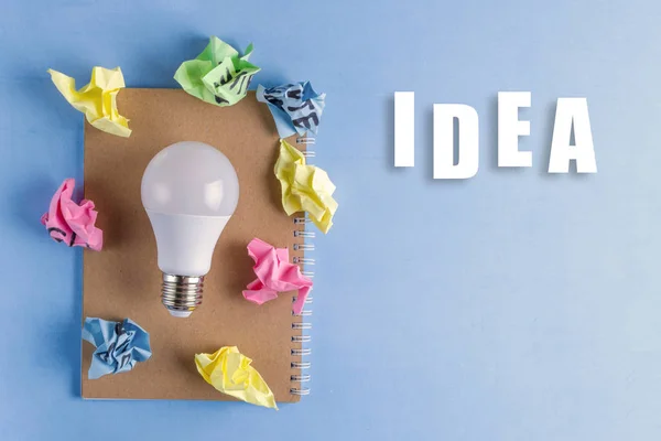 Idea concept. New idea. Colorful crumpled paper balls, notebook and light bulb on a blue background. Start up