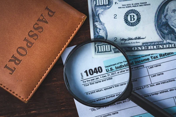 Payment of taxes. Filling by the taxpayer of the tax form 1040. Tax return, passport, american hundred dollars and magnifier on a wooden table. Tax concept.