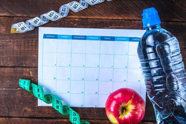 Drawing up and planning a program of sports training and diet. Sports and healthy lifestyle. An apple, a bottle of water, a measuring tape on a wooden background. Sport and diet concept 