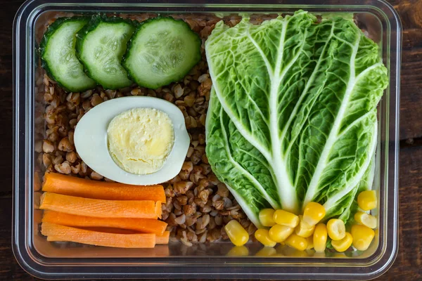 Healthy meal in a plastic container. Snack in the office, at work. Lunch box of cucumbers, buckwheat, carrots, eggs, lettuce and canned corn. Nutrition and healthy food concept