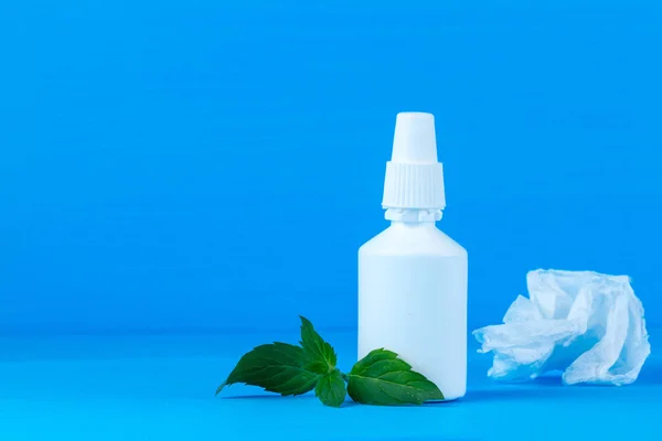 Spray from the common cold and a mint on a blue background. Cold treatment. Medication from stuffy nose. Throw off an illness