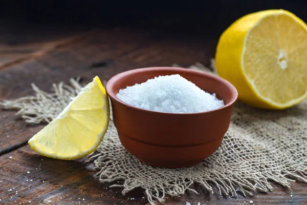 Lemon acid in a brown, small plate, a slice of lemon and a juicy lemon on a wooden background. Citric acid