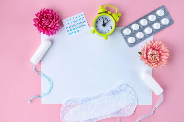 Tampons for menstruation, alarm clock, women\'s calendar, feminine pads, pain pills for critical days and flowers on a pink background. Hygiene care during critical days. Regular menstrual cycle. Copy space