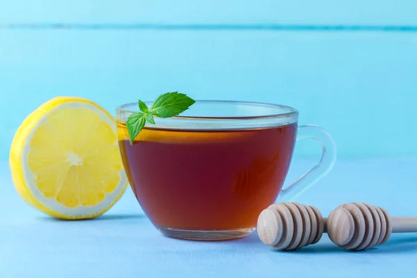 お茶を飲みます 新鮮なミントと青の背景にジューシーなレモン蜂蜜スプーンのスライスと熱いお茶のカップ — ストック写真