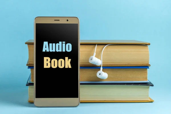 Headphones, mobile phone and books on a blue background. Audio book concept. Play audio playback of literary, educational books.