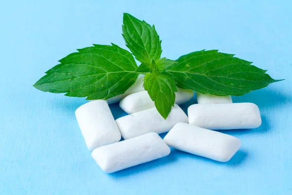 Chewing gum with a piece of fresh mint on a blue background. Fresh breath, mint chewing gum