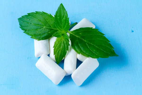 Chewing gum with a piece of fresh mint on a blue background. Fresh breath, mint chewing gum