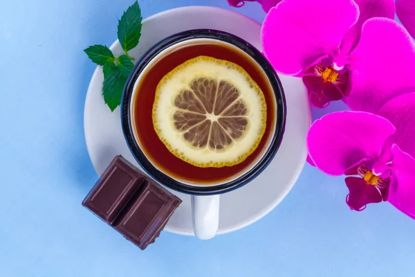 レモン 蘭の花 フレッシュミント青の背景にチョコレートと紅茶 居心地の良い週末と娯楽 平面図です 紅茶ドリンク — ストック写真