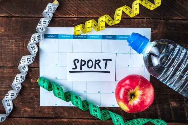 Drawing up and planning a program of sports training and diet. Sports and healthy lifestyle. An apple, a bottle of water, a measuring tape on a wooden background. Motivation. Sport and diet concept