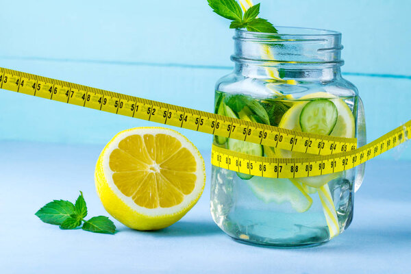 Diet concept. Detox drinks. Lemon water, juicy lemon, mint and measuring tape on a blue background. Detox 