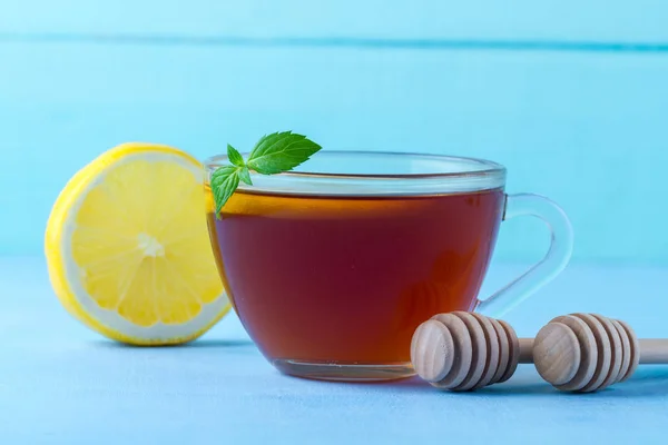 お茶を飲みます 新鮮なミントと青の背景にジューシーなレモン蜂蜜スプーンのスライスと熱いお茶のカップ — ストック写真