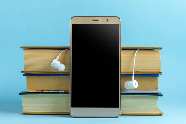 Headphones, mobile phone and books on a blue background. Audio book concept. Reading books without looking up from work
