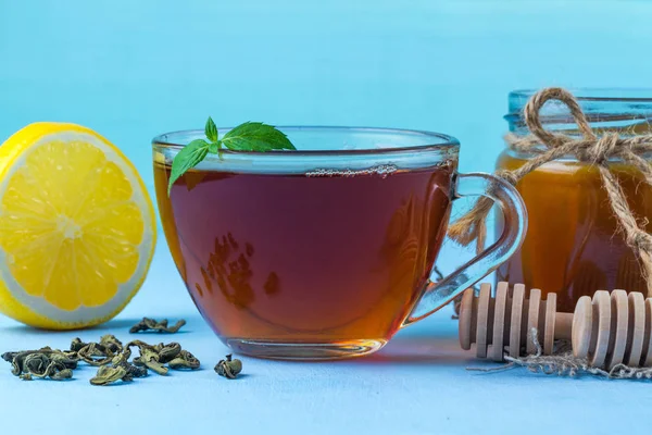 新鮮なミント ジューシーな黄色のレモン 自家製蜂蜜の瓶 青の背景に蜂蜜スプーンのスライスと熱いお茶のカップ お茶を飲む — ストック写真