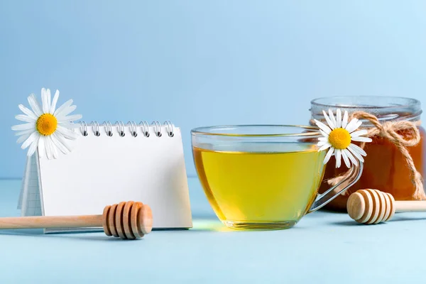 Chamomile tea. Chamomile flowers, honey, place for text and a cup of chamomile tea on a blue background. Copy space