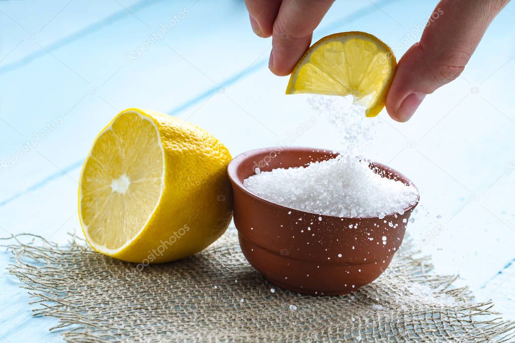 Lemon acid in a brown, small plate, a slice of lemon in hands and a juicy lemon on a wooden background. Citric acid. 