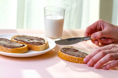 Taze pişmiş ekmek üzerinde çikolatalı hamur yayılır. Somun, tatlı hamur ve bir bardak süt bir kahvaltı için çikolatalı sandviç. 