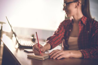 Genç, çekici kadın bir not defterini içinde online evde bir dizüstü bilgisayarda çalışırken alır. 