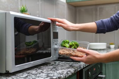 Gıda Isıtma için mikrodalga fırın kullanarak. Bir plastik konteyner ile brokoli ve buğday mikrodalga ısı olacak kadın eli 