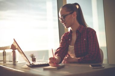 Genç, çekici kadın bir not defterini içinde online evde bir dizüstü bilgisayarda çalışırken alır. 