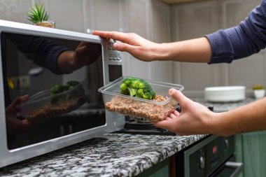 Gıda Isıtma için mikrodalga fırın kullanarak. Bir plastik konteyner ile brokoli ve buğday mikrodalga ısı olacak kadın eli 