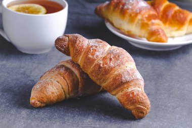 Taze pişmiş kruvasanlar ve geleneksel Fransız kahvaltı karanlık bir arka plan üzerinde için Limonlu sıcak çay. Ekmek yapım ürünleri