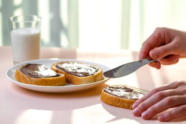 Taze pişmiş ekmek üzerinde çikolatalı hamur yayılır. Somun, tatlı hamur ve bir bardak süt bir kahvaltı için çikolatalı sandviç. 