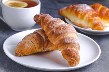 Taze pişmiş kruvasanlar ve geleneksel Fransız kahvaltı karanlık bir arka plan üzerinde için Limonlu sıcak çay. Ekmek yapım ürünleri