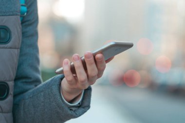 Kadın bir cep telefonu şehrin arka plan üzerinde tutuyor. Mobil iletişim ve uygulamaları. Telefon ve sosyal ağlar üzerinde bağımlılık