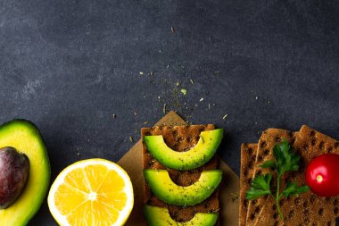 Avokado ile net sandviç. Aperatif ekmek ve fitness yeme. Çavdar, buğday gevrek ekmek, pirinç ekmek ve limon, maydanoz, domates karanlık bir arka plan üzerinde. Düz yatıyordu 