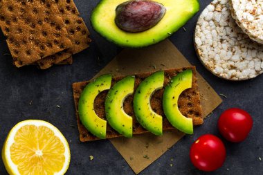 Avokado ile net sandviç. Aperatif ekmek ve fitness yeme. Çavdar, buğday gevrek ekmek, pirinç ekmek ve limon, maydanoz, domates karanlık bir arka plan üzerinde. Düz yatıyordu 