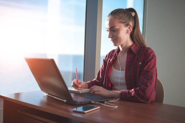Online eğitim hizmetini kullanarak öğrenci. Eğitim yabancı dil kursları ve kulaklık ile dinleme izlerken laptop ekranında arayan genç kadın. Modern çalışma teknoloji kavramı. 