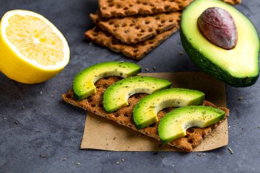 Avokado ile net sandviç. Aperatif ekmek ve fitness yeme. Çavdar, buğday gevrek ekmek, pirinç ekmek ve limon, maydanoz, domates karanlık bir arka plan üzerinde. Düz yatıyordu 