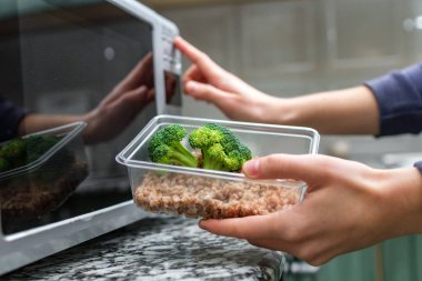 Gıda Isıtma için mikrodalga fırın kullanarak. Bir plastik konteyner ile brokoli ve buğday mikrodalga ısı olacak kadın eli 