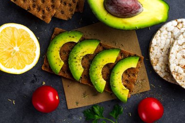 Avokado ile net sandviç. Aperatif ekmek ve fitness yeme. Çavdar, buğday gevrek ekmek, pirinç ekmek ve limon, maydanoz, domates karanlık bir arka plan üzerinde. Düz yatıyordu 