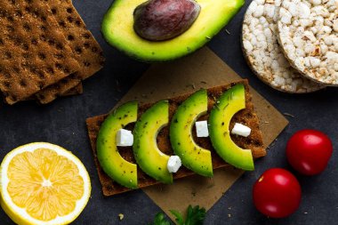 Avokado ile net sandviç. Aperatif ekmek ve fitness yeme. Çavdar, buğday gevrek ekmek, pirinç ekmek ve limon, maydanoz, domates karanlık bir arka plan üzerinde. Düz yatıyordu 
