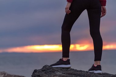 Kayalar bir egzersiz yaptıktan sonra bir deniz arka plan üzerinde günbatımında tırmanma spor ayakkabı kadın. Spor ve aktif yaşam tarzı
