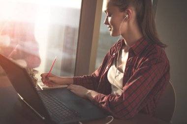 Online eğitim hizmetini kullanarak öğrenci. Eğitim yabancı dil kursları ve çekici notlar not defterinde izlerken laptop ekranında arayan genç kadın. Modern çalışma teknoloji kavramı. 