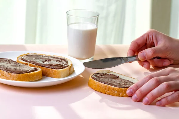 Spread chocolate paste on freshly baked bread. Chocolate sandwiches with nut, sweet paste and a glass of milk for a breakfast.