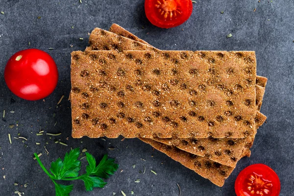 Rye and wheat crisp bread, cherry tomatoes and fresh parsley on a dark background. Snack Bread. Top view