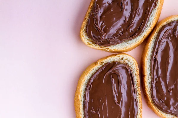 Pieces of loaf with chocolate paste on a pink background. Chocolate sandwiches with nut paste on a breakfast. Top view. Copy space