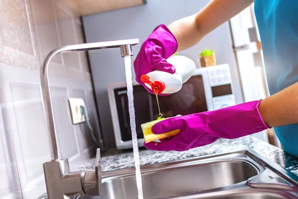 Housewife in rubber colored gloves washing dishes with a yellow sponge in the kitchen at home.