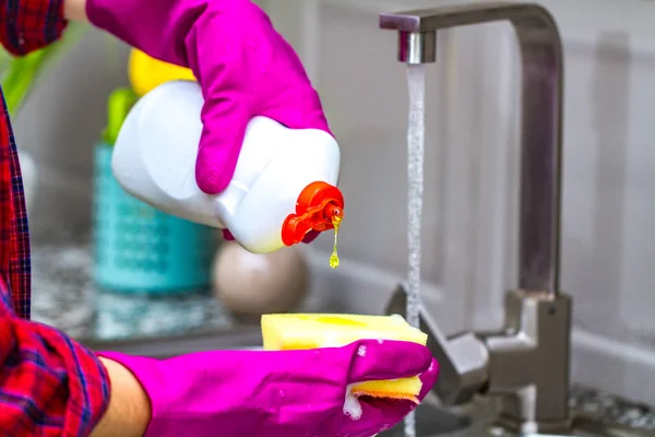 Woman in rubber colored gloves washing dishes in kitchen. Close up of housewife hands.