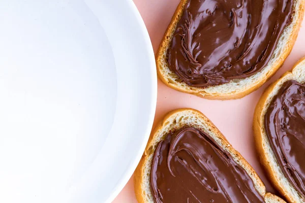 Pieces of loaf with chocolate paste and a plate on a pink background. Chocolate sandwiches with nut paste on a breakfast. Top view. Copy space