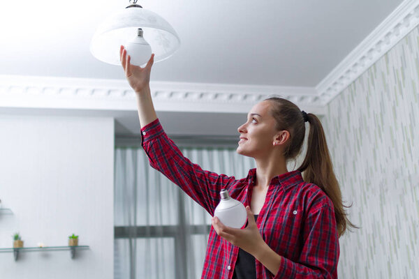 Young, attractive housewife makes the replacement of the used LED light bulb in the chandelier in the room 