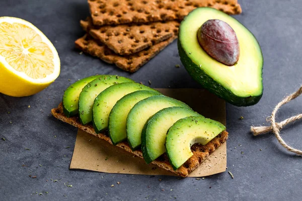 Crisp sandwich with avocado. Snack Bread and fitness eating. Rye, wheat crisp bread, rice bread and lemon, parsley, cherry tomatoes on a dark background. Flat lay