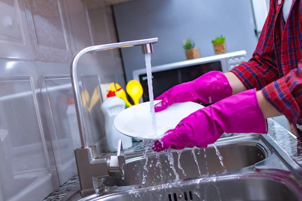 Housewife in rubber colored gloves washing dishes with a yellow sponge in the kitchen at home.