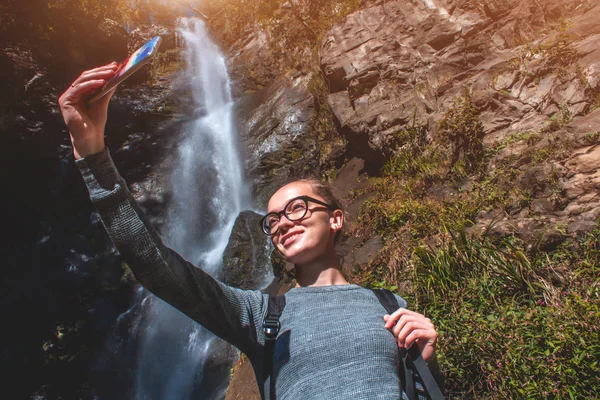 若い女の子の旅行者が山の中の滝で写真を取る 美しい風景の背景の写真 — ストック写真