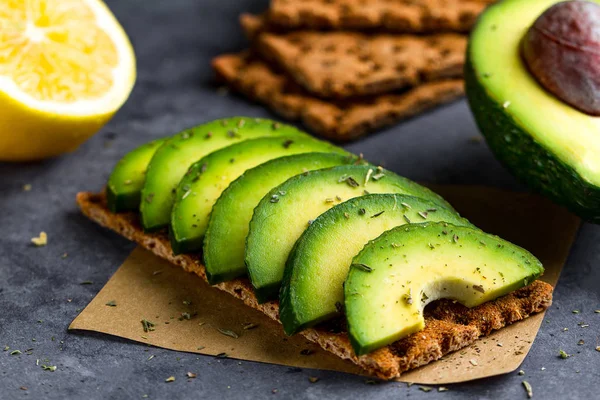 Crisp sandwich with avocado. Snack Bread and fitness eating. Rye, wheat crisp bread, rice bread and lemon, parsley, cherry tomatoes on a dark background. Flat lay