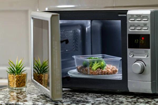 Using the microwave oven to heat food. Heating plastic container with broccoli and buckwheat in the microwave